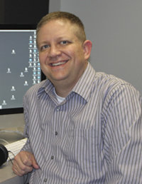 A smiling man sitting at a computer.