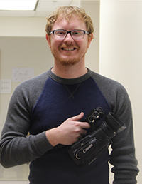 A smiling man holding a video camera.